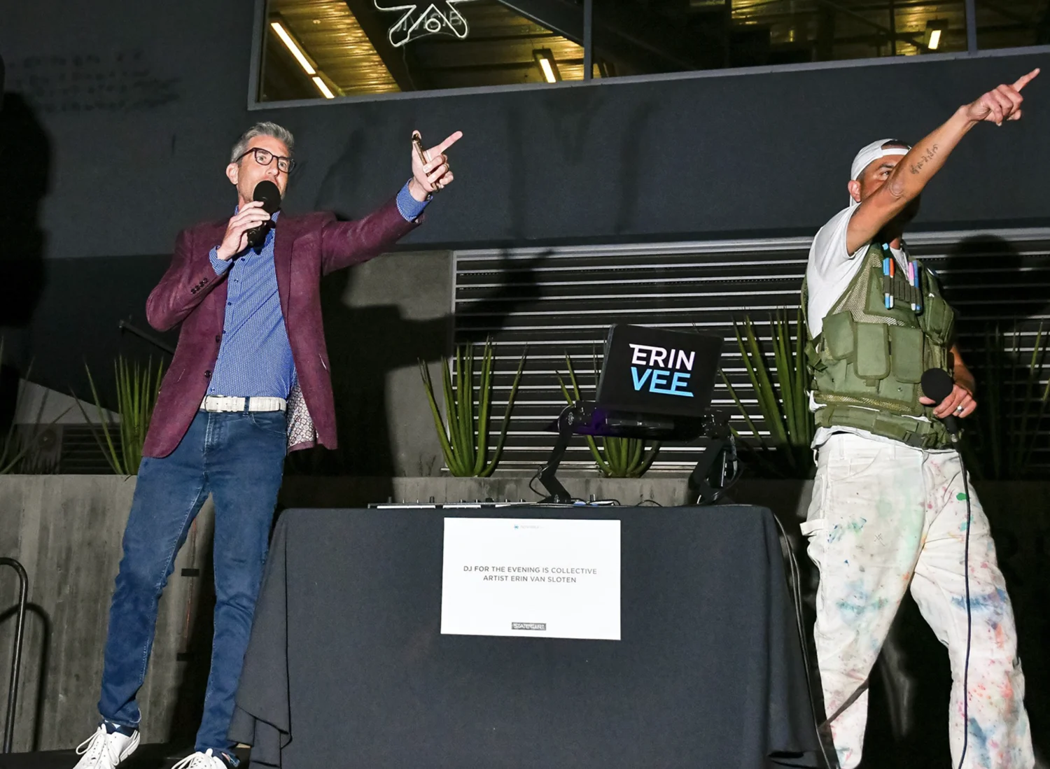 Hosts on the mic beside the DJ table and its State of the Art sign