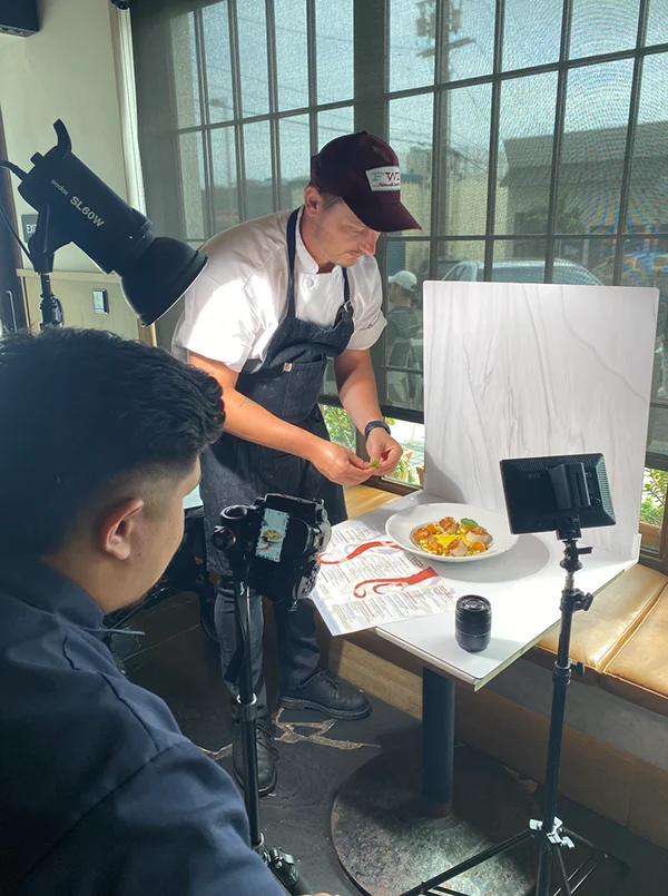 Behind the scenes: a chef plates a dish for a lit tabletop shoot while the photographer frames it